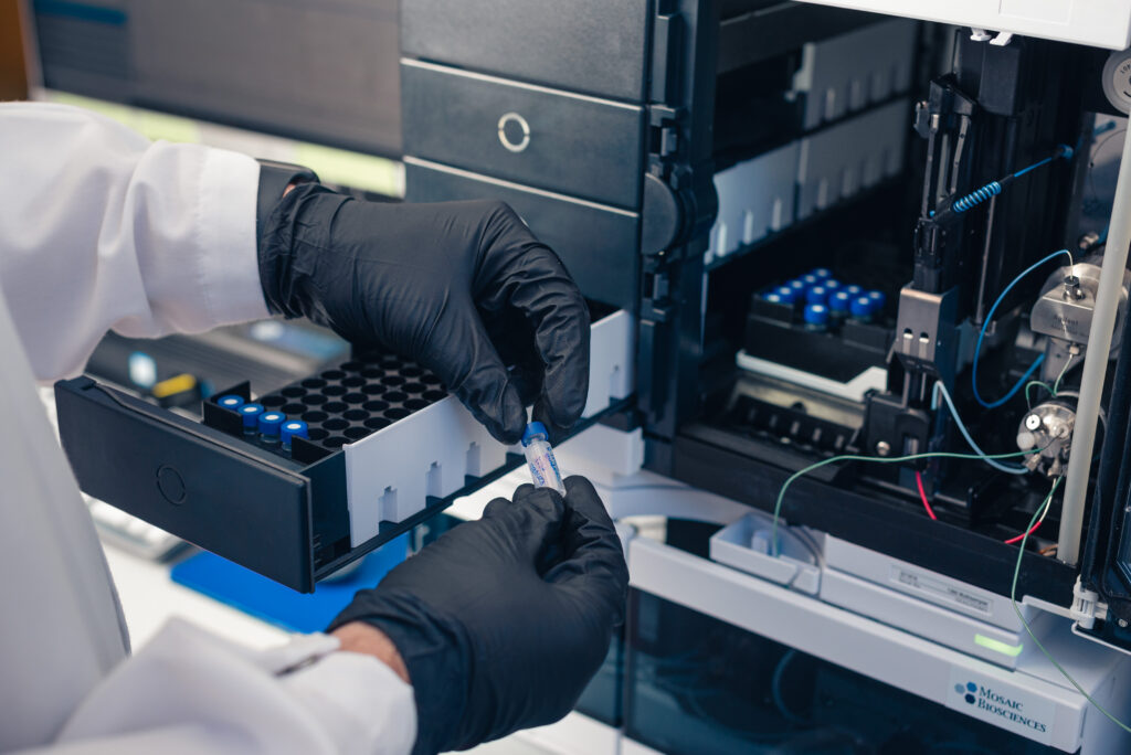 Scientist handling a sample vial while loading a laboratory instrument for biologic discovery experiments.