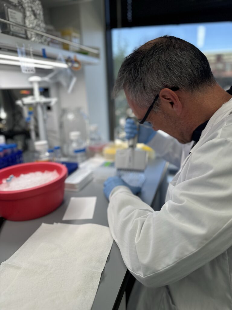Scientist performing pipetting and sample preparation at a laboratory bench during biologics discovery research.